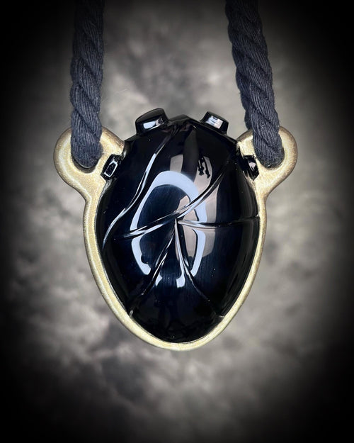 Black obsidian crystal handmade gemstone carved into an anatomical human heart shape and sculpted into a necklace with a gold finish. Hung from cotton ropes for sustainable elegance. 